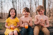 Trois enfants assis sur un mur dégustant des boissons estivales — Photo de stock