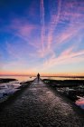 Silhueta de mulher em pé no molhe por mar, céu púrpura por do sol — Fotografia de Stock