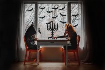 Двое детей в костюмах Хэллоуина сидят у окна, делая паб, США — стоковое фото