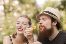 Couple sitting in a park holding a bubble wand blowing bubbles — Stock Photo