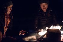 Duas mulheres sentadas ao redor de um acampamento tostam marshmallows — Fotografia de Stock