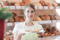 Улыбающийся помощник по продажам в пекарне с подносом образцов — стоковое фото
