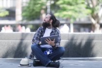 Homem sentado em seu skate usando um tablet digital — Fotografia de Stock