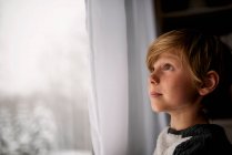 Garçon regardant par la fenêtre en hiver — Photo de stock