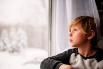 Boy looking out of the window in winter — Stock Photo