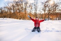 Garçon assis dans la neige avec les bras levés — Photo de stock