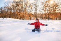 Хлопчик сидить на снігу з витягнутими руками — стокове фото