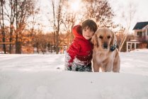 Портрет мальчика, сидящего в снегу со своей золотой ретривер-собакой — стоковое фото