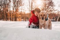 Портрет мальчика, сидящего в снегу со своей золотой ретривер-собакой — стоковое фото