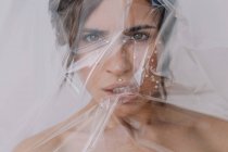 Retrato de uma mulher com pérolas no rosto envolto em plástico transparente — Fotografia de Stock