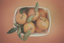Vista aérea de un punnet de mandarinas, fondo naranja - foto de stock
