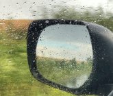 Close-up de um espelho de asa através de uma janela de carro molhado — Fotografia de Stock