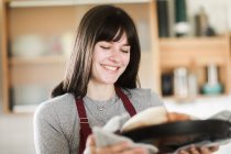 Mujer sonriente de pie en la cocina sosteniendo un pan recién horneado - foto de stock