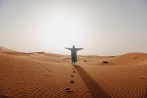 Hombre de pie en el desierto del Sahara con las armas extendidas, Marruecos - foto de stock