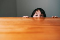 Mädchen versteckt sich hinter einem Tisch — Stockfoto