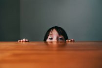 Ragazza che si nasconde dietro un tavolo — Foto stock