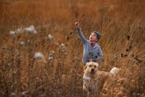 Boy standing in a field with his dog holding long grass, United States — Stock Photo