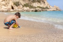 Menino enchendo um balde com areia na praia, Grécia — Fotografia de Stock