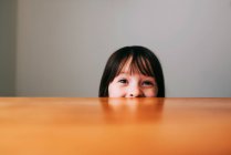 Chica escondida detrás de una mesa - foto de stock