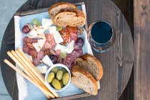 Vista aérea de queijo, charcutaria, azeitonas, uvas e pão numa mesa com um copo de vinho tinto — Fotografia de Stock