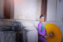 Retrato de una mujer con ropa tradicional tailandesa apoyada en un edificio, Tailandia - foto de stock