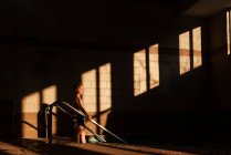 Garçon debout sur les marches d'une piscine dans l'ombre — Photo de stock
