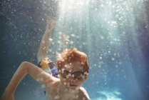 Primer plano de un niño nadando bajo el agua en una piscina - foto de stock