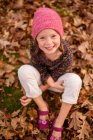 Chica sonriente sentada entre hojas de otoño, Estados Unidos - foto de stock