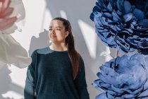 Портрет жінки, що стоїть поруч з гігантськими штучними квітами — стокове фото