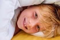Portrait d'un garçon souriant couché au lit — Photo de stock