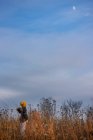 Girl standing in a field looking up at the evening moon, United States - foto de stock