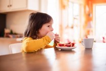 Mädchen sitzt an einem Tisch und isst eine Blutorange — Stockfoto