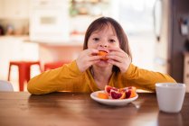 Девушка сидит за столом и ест кровавый апельсин — стоковое фото