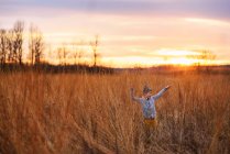 Boy standing in a field with his arms in the air, United States - foto de stock