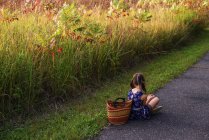 Fille assise jambes croisées par un champ avec un panier, États-Unis — Photo de stock