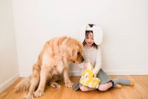 Retrato de una chica sonriente con orejas de conejo sentada en el suelo con su perro - foto de stock