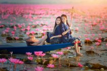 Dos mujeres sentadas en un barco en un lago de flores de loto, Tailandia - foto de stock