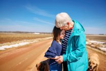 Abuela parada junto a un camino con dos perros abrazando a su nieta, Estados Unidos - foto de stock