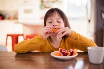 Menina sentada em uma mesa comendo uma laranja de sangue — Fotografia de Stock