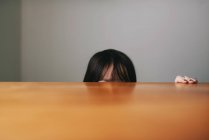 Девушка прячется за столом, обрезанный образ — стоковое фото