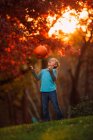 Boy standing in the garden throwing a pumpkin in the air, United States — Stock Photo