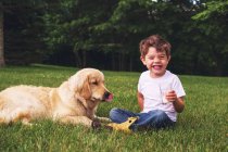 Boy sitting outdoors drinking a glass of milk with a golden retriever — Stock Photo