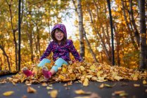 Chica sonriente sentada en una pila de hojas de otoño en un trampolín, Estados Unidos - foto de stock