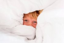 Porträt eines Jungen, der sich in einer Bettdecke versteckt — Stockfoto