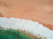 Повітряний вид на падіння пінистої хвилі на пляжі — стокове фото