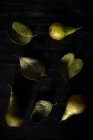 Pere disposte su foglie sopra tavolo nero — Foto stock