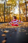 Menino sentado de pernas cruzadas em um trampolim coberto em folhas de outono, Estados Unidos — Fotografia de Stock