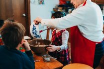 Two children helping their grandmother bake a cake — Stock Photo
