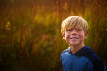 Retrato de un niño sonriente parado en un campo al atardecer, Estados Unidos - foto de stock