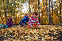 Three children playing on a trampoline covered in autumn leaves, United States — Stock Photo